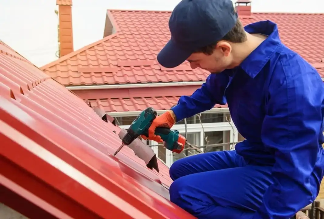 Muncitor profesionist la lucru pe acoperiș cu țiglă metalică roșie - servicii constructii acoperisuri